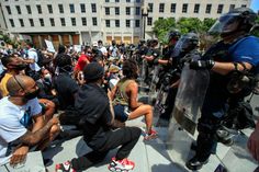 a group of people sitting on the ground with police standing behind them and holding onto their skateboards