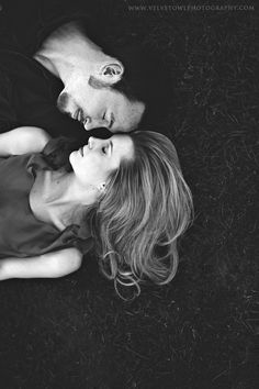 a man and woman laying on the ground with their heads close to each other looking at something