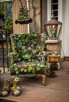 a chair covered in plants sitting on the side of a building next to a lamp