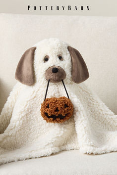 a stuffed dog with a pumpkin in its mouth on a white blanket that says pottery barn