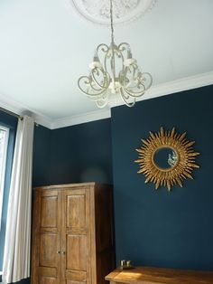 a bedroom with blue walls and a gold sun mirror hanging on the wall next to a wooden dresser