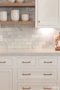 a kitchen with white cabinets and marble counter tops, gold pulls on the cupboards