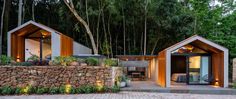 two small houses are built into the side of a stone wall and surrounded by greenery