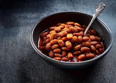 a bowl filled with baked beans on top of a black tablecloth next to a spoon