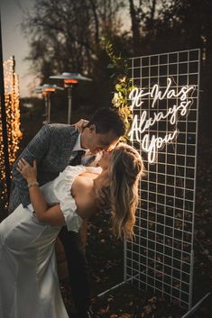 a bride and groom kissing in front of a neon sign