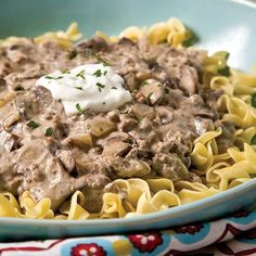 a blue bowl filled with pasta and meat covered in gravy on top of a table