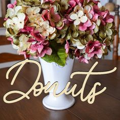 a vase filled with lots of flowers on top of a wooden table next to a sign that says donuts