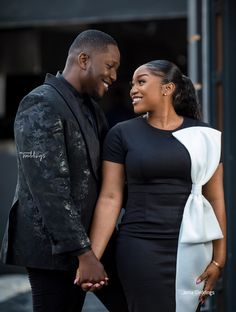 a man and woman standing next to each other in front of a building smiling at each other