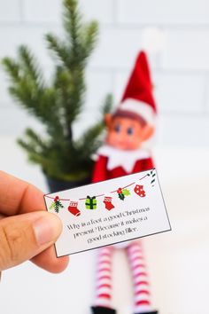 an elf is holding up a business card for someone to put on their christmas tree