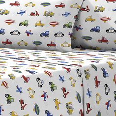 a bed covered in white sheets with colorful vehicles on them and matching pillowcases