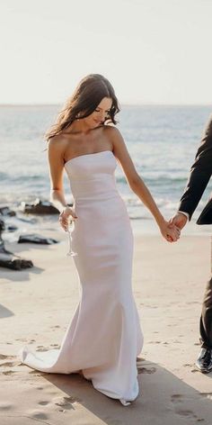 a bride and groom holding hands on the beach