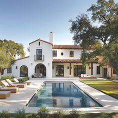 a large white house with a pool and lounge chairs in the front yard, surrounded by trees