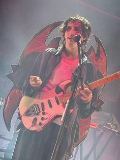 a man holding a guitar while standing in front of a microphone on top of a stage