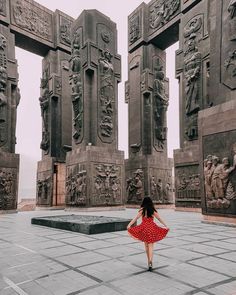 a woman in a red and white dress is walking through a monument