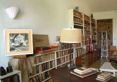 a living room filled with lots of books on top of a wooden table next to a lamp