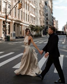 a man and woman are walking across the street holding hands while dressed in formal attire