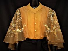 a woman's yellow top with gold flowers and leaves on the front, sitting on a black mannequin