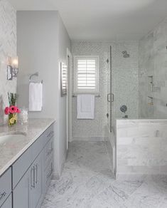 a white bathroom with marble counter tops and gray cabinets, along with a walk in shower