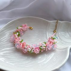 a white plate with pink flowers and green beads on the edge, next to a gold chain