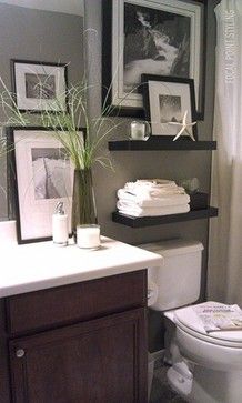 a bathroom with pictures on the wall above the toilet and towels stacked on the shelf