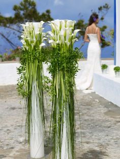 two white vases with flowers in them on the ground near a bride and groom