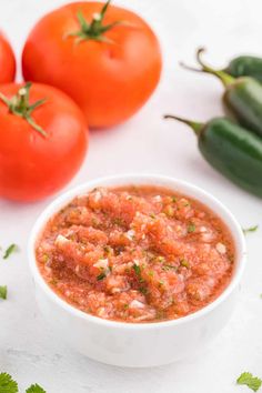 a white bowl filled with salsa next to tomatoes