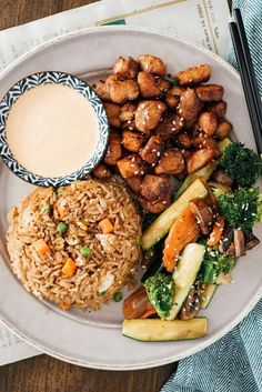 a white plate topped with rice, broccoli and chicken next to a bowl of sauce