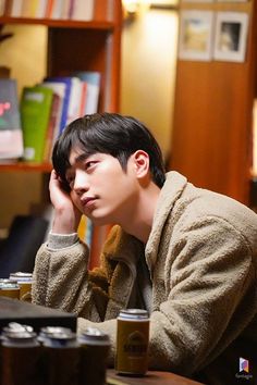 a young man sitting at a table with his hand on his head and looking off to the side