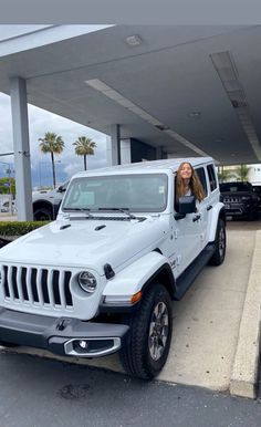 a woman sitting in the driver's seat of a white jeep at a gas station