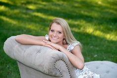 a woman sitting on top of a gray chair in the grass with her legs crossed