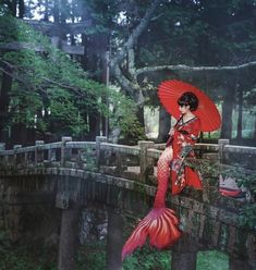 a woman in a red kimono holding an umbrella over her head while standing on a bridge