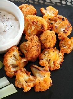 some cauliflower and celery on a black plate with a small white bowl