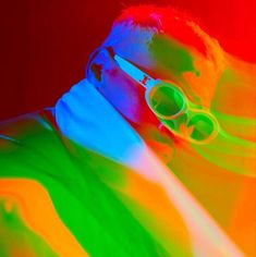 a man with sunglasses on his face and in the background is an image of multicolored light