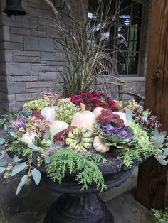 an arrangement of flowers and pumpkins in a black vase sitting on a pedestal outside