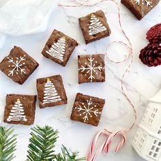 brownies decorated with christmas trees and snowflakes sit on a marble surface next to candy canes