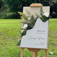 a welcome sign with flowers and greenery on it sitting in the middle of a field