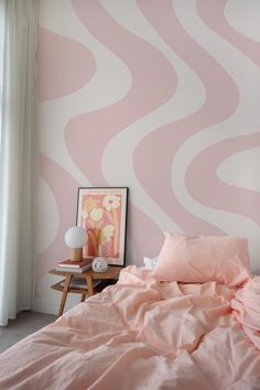 a bed with pink sheets and pillows in front of a wall painted with wavy lines