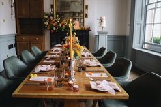 a long wooden table with place settings and candles on it in front of a fireplace