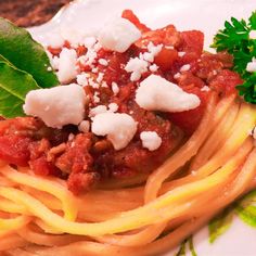 a plate of spaghetti with sauce, cheese and parmesan on the side next to a leafy green garnish