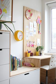 a desk with two white chairs in front of a window next to a book shelf