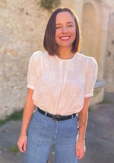 a woman standing in front of a stone building with her hands in her pockets and smiling at the camera