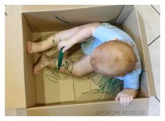 a young boy is playing with green crayons in a cardboard box