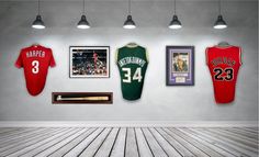 three baseball jerseys hanging on the wall in a room with wooden floors and framed pictures