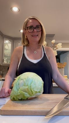 a woman standing in front of a cutting board with a head of cabbage on it