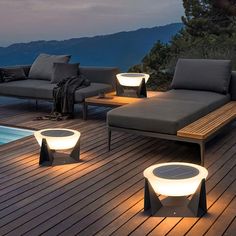 modern outdoor furniture is lit up at night on the deck near a swimming pool with mountains in the background