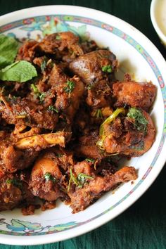 a white plate topped with meat covered in sauce and garnished with green leaves