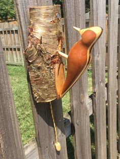 a wooden bird is perched on a fence post and has its head stuck in the tree