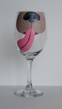 a wine glass with a dog's face painted on the side and a pink piece of paper sticking out of it