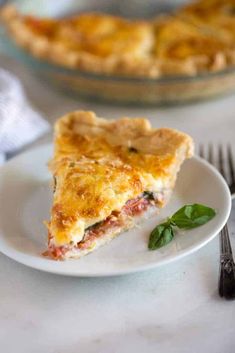 a slice of quiche on a plate next to a fork and glass pie dish