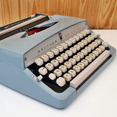 an old blue typewriter sitting on top of a white table next to a wooden wall